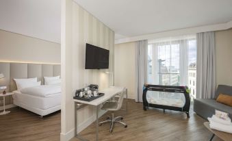 a modern hotel room with a bed , desk , and tv , as well as a baby crib in the corner at NH Leipzig Zentrum
