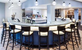 a modern bar with a curved counter and several stools , along with various bottles and glasses on the counter at Delta Hotels Milton Keynes