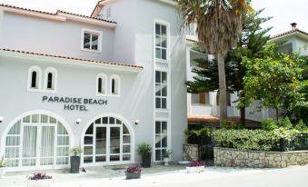"a white building with a sign that reads "" paradise beach hotel "" is shown next to a palm tree" at Paradise Beach Hotel