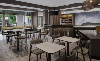 a modern , well - lit restaurant with wooden tables and chairs arranged in an open space , offering a variety of seating options at SpringHill Suites Tuckahoe Westchester County