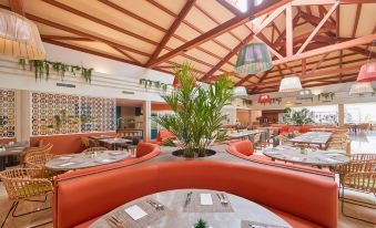 a restaurant with orange booths , white tablecloths , and green plants under a wooden ceiling , giving it an inviting atmosphere at Zafiro Can Picafort