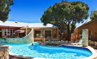 a large swimming pool with people in it , surrounded by a building and trees , under a clear blue sky at Karma Rottnest