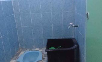 a bathroom with blue tile walls , a black trash can , and a blue basin , all in front of a window at Penginapan Rindu Alam Soala Gogo