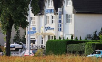 "a white building with a sign that reads "" hotel "" on it , surrounded by trees and grass" at Falkensee