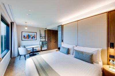 a modern bedroom with a large bed , white walls , and a dining table in the corner at Oval Hotel at Adelaide Oval, an EVT hotel