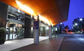 a modern building with a wooden roof and large windows , illuminated by lights , at dusk at Novotel Canberra