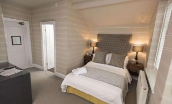 a large bed with white linens and a gray headboard is in a room with two lamps at The Bear, Cowbridge