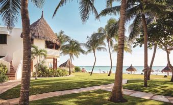 a tropical resort with thatched - roof buildings , palm trees , and a clear blue sky , along with a grassy area leading to the beach at Chable Maroma