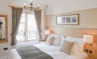 a large bed with white linens and a gray blanket is situated in a room with a window , framed pictures on the wall , and lamps at The New Inn