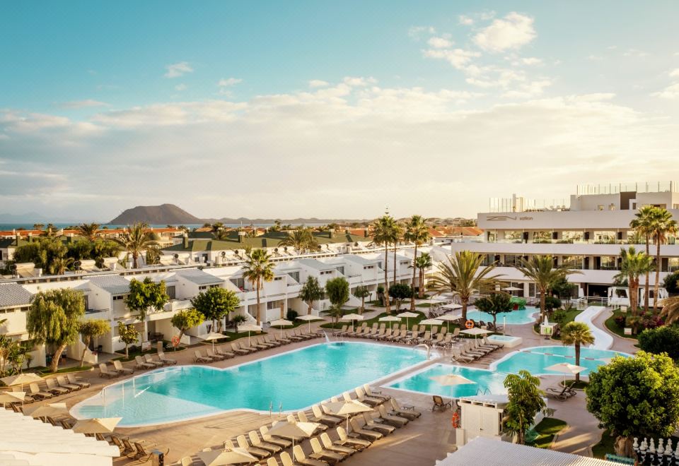 a large swimming pool surrounded by palm trees and buildings , with a clear blue sky overhead at Playa Park Zensation