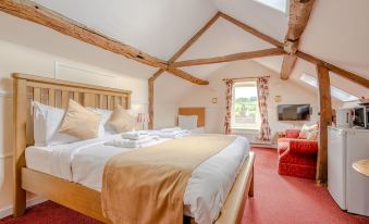 a spacious bedroom with wooden beams on the ceiling , a large bed , and a red couch at The Crown Hotel