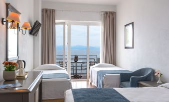 a hotel room with two beds , a tv , and a balcony overlooking the ocean , all set against a white wall at Louis Ionian Sun