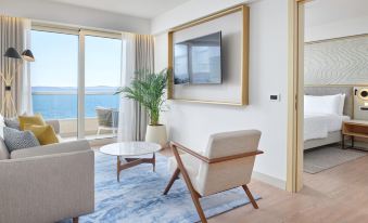 a living room with a large window overlooking the ocean , a flat - screen tv on the wall , and a wooden chair and a potted plant at Le Méridien Lav, Split