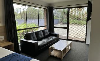a living room with a black leather couch , wooden coffee table , and large windows overlooking a tennis court at Logan City Motor Inn