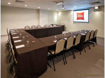 a conference room with a large table , chairs , and a tv displaying an advertisement for ibis hotels at Ibis Melbourne Hotel and Apartments