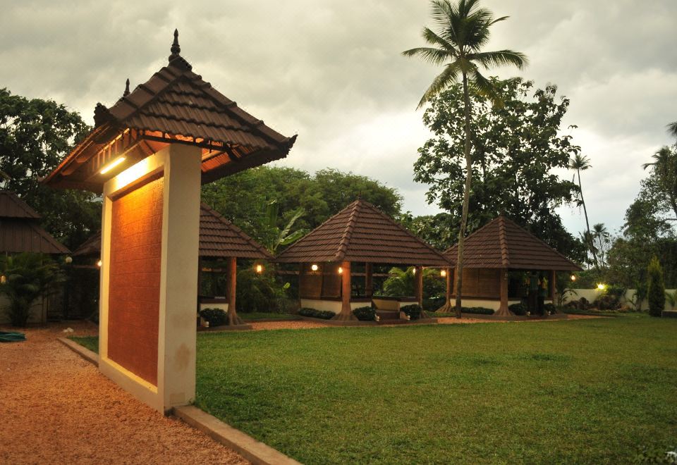 a grassy area with three thatched - roof houses , one of which has a green light shining on it at The Palms Hotel