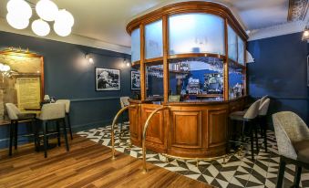 a bar area with a curved wooden counter and chairs , surrounded by blue walls and patterned flooring at Bredbury Hall Hotel