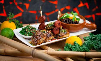 a white plate filled with various skewered meats , vegetables , and a bowl of rice , accompanied by a fork and knife at Pacific Hotel Cairns