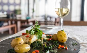 a plate of food with potatoes , herbs , and a glass of white wine on a table at Belmar Spa & Beach Resort