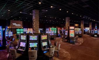 a large casino with multiple slot machines and gaming tables , along with people playing games at Angel of the Winds Casino Resort