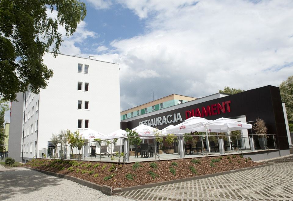 "a white building with a sign that reads "" restauracja "" and umbrellas , surrounded by trees and grass" at Hotel Diament Zabrze - Gliwice