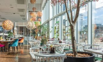 an indoor dining area with white tables and chairs , surrounded by large windows and trees at Radisson Blu Hotel Uppsala