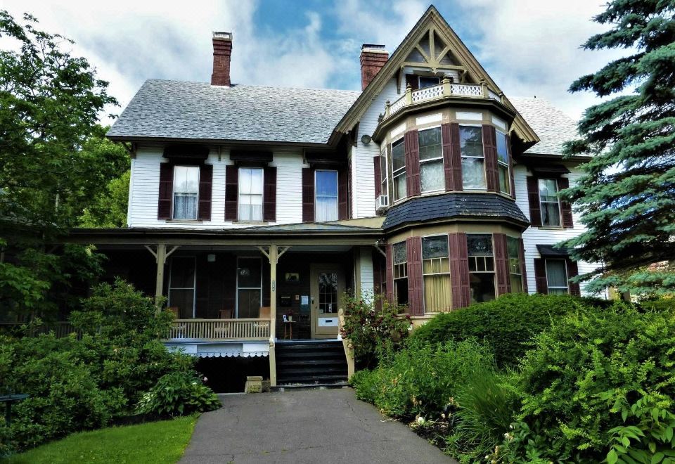 a large , two - story victorian - style house with a large porch and balcony , surrounded by lush greenery at Black Swan Inn