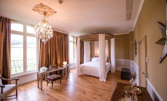 a spacious bedroom with a four - poster bed , a chandelier hanging from the ceiling , and wooden floors at Chateau de Sacy