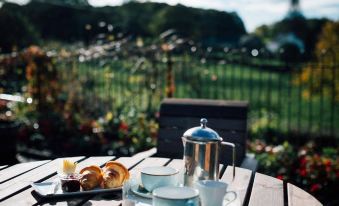 a table with a teapot , cups , and pastries is set up outside near a garden at The Brown Horse Inn