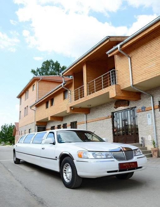 a white limousine is parked in front of a building with a balcony , surrounded by trees at Alfa Hotel