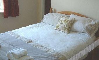 a neatly made bed with white sheets and pillows , set against a beige wall with a window at The Royal Oak