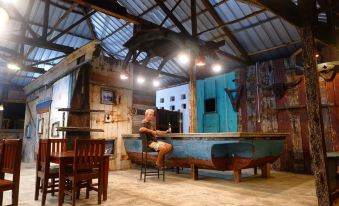 a man is sitting at a bar in an old barn with wooden furniture and a blue boat at Rock and Wreck Dive Resort