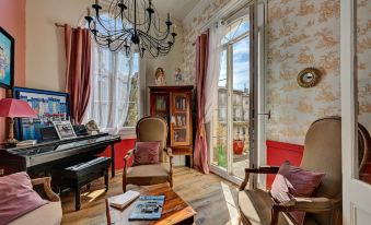 a cozy living room with a grand piano , wooden floors , and large windows , decorated in red and white color scheme at Hotel des Artistes