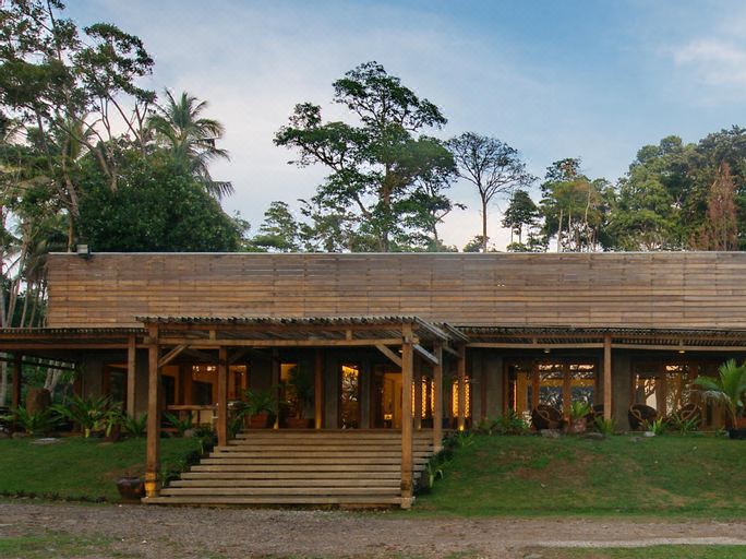 a wooden building with a sloping roof , surrounded by trees and bushes , under a blue sky at The Pade Dive Resort