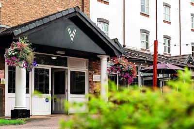 "a brick building with a sign that reads "" v "" on the front , surrounded by greenery and flowers" at Village Hotel Liverpool