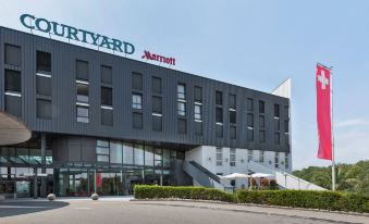 "a modern hotel building with the name "" courtyard by marriott "" on top of it , surrounded by trees and grass" at Courtyard Basel