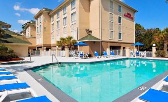a large swimming pool with lounge chairs and umbrellas in front of a hotel building at Hilton Garden Inn Hilton Head