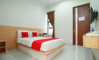 a large bed with a wooden headboard and white sheets is in a room with a door at RedDoorz Syariah Near Universitas Jenderal Soedirman
