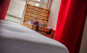 a bedroom with a bed , red curtains , and a basket of items near the window at The Howard Arms