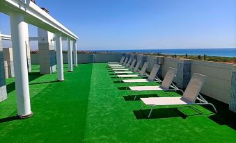 a rooftop patio overlooking the ocean , with numerous lounge chairs and umbrellas placed on it at Hotel Vent de Mar