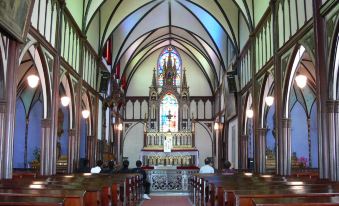 a church interior with people sitting at wooden pews and a large stained glass window at Nagasaki Nisshokan
