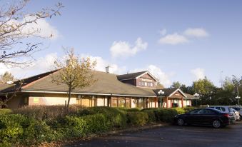 a large building with a brown roof and beige walls is surrounded by trees and bushes at Premier Inn Liverpool (Tarbock)