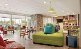 a modern living room with a green couch , wooden dining table , and several chairs arranged around it at Home2 Suites by Hilton Williamsville Buffalo Airport