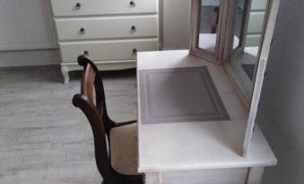 a white wooden dresser with a mirror on top , and a wooden chair placed next to it at Guest House