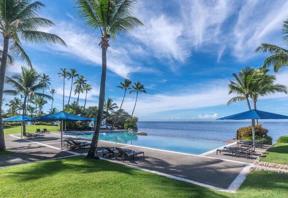 a beautiful tropical resort with a swimming pool , umbrellas , and palm trees near the ocean at Shangri-La Yanuca Island, Fiji