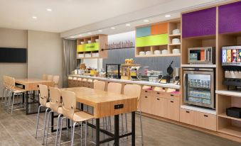 a modern kitchen with wooden tables , chairs , and various appliances , including a toaster , oven , and coffee maker at Home2 Suites by Hilton Harrisburg North