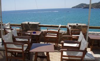 a patio with wooden furniture and a view of the ocean , surrounded by rocks and umbrellas at Argo Spa Hotel