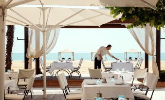 a man is setting up an outdoor dining area near the ocean , serving tables and chairs at Mediterranean Village Hotel & Spa