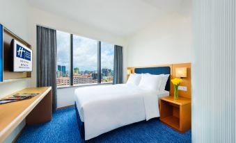 A bedroom with large windows and a balcony that overlooks the city, featuring an unmade bed at Holiday Inn Express Macau City Centre