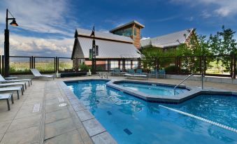 an outdoor pool with a hot tub and lounge chairs , surrounded by trees and a building at Newpark Resort